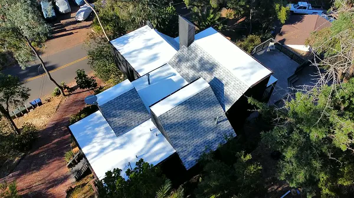 Aerial drone view of a completed home re-roof surrounded by mature trees in San Diego