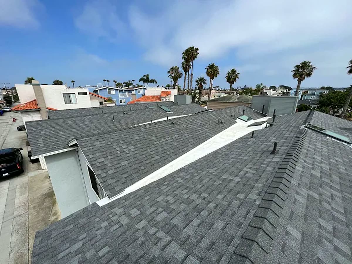 Completed gray shingle roof with the San Diego coastal skyline and palm trees behind it