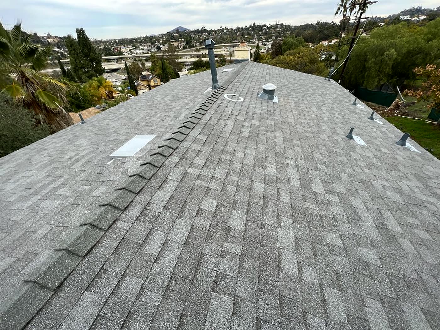 Newly installed gray asphalt shingle roof ridge with the San Diego hills in the background